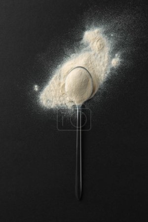 Spoon of agar-agar powder on black background, top view