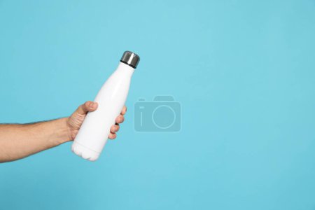 Téléchargez les photos : Homme tenant une bouteille thermo sur fond bleu clair, gros plan. Espace pour le texte - en image libre de droit