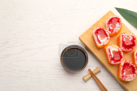 Foto de Deliciosos rollos de sushi con salmón, palillos y salsa de soja en la mesa de madera blanca, puesta plana. Espacio para texto - Imagen libre de derechos