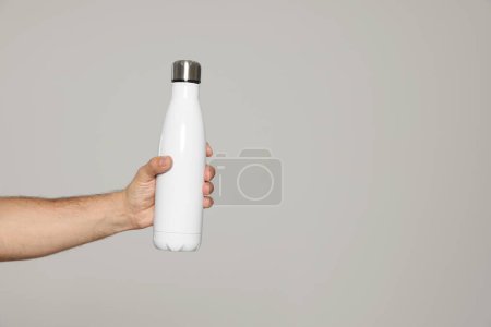 Téléchargez les photos : Homme tenant une bouteille thermo sur fond gris clair, gros plan. Espace pour le texte - en image libre de droit