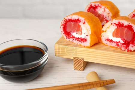 Foto de Deliciosos rollos de sushi con salmón, palillos y salsa de soja en la mesa de madera blanca, primer plano - Imagen libre de derechos