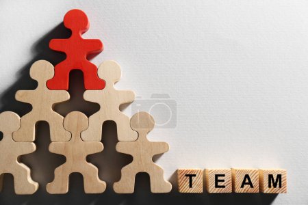 Red figure among wooden ones and cubes with word Team on white background, flat lay with space for text. Recruiter searching employee