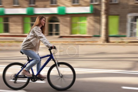 Happy beautiful woman riding bicycle in city, motion blur effect