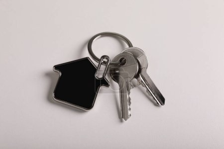 Keys with trinket in shape of house on white background, above view. Real estate agent services