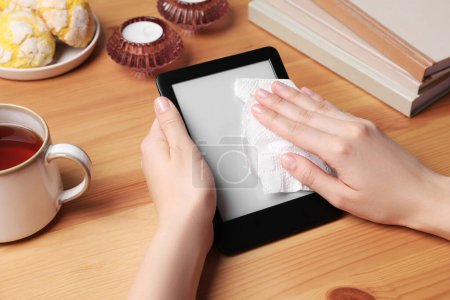 Téléchargez les photos : Woman wiping smartphone with paper at wooden table, closeup - en image libre de droit