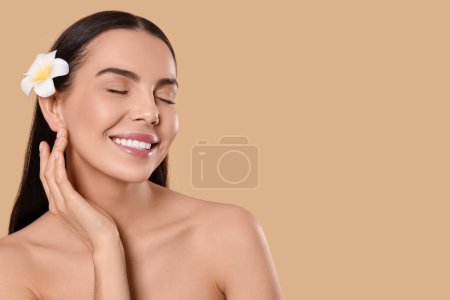 Photo for Young woman with plumeria flower in hair on beige background, space for text. Spa treatment - Royalty Free Image