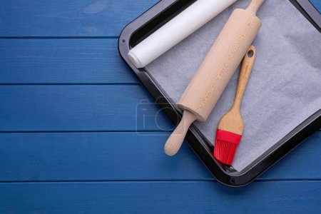 Téléchargez les photos : Baking parchment papers, rolling pin and brush on blue wooden table, flat lay. Space for text - en image libre de droit