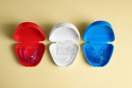 Transparent dental mouth guards in containers on beige background, flat lay. Bite correction