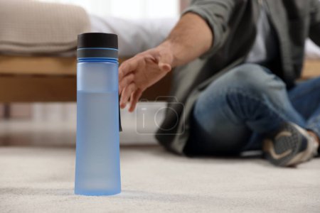Téléchargez les photos : Man taking transparent plastic bottle with water while sitting on floor at home, closeup - en image libre de droit