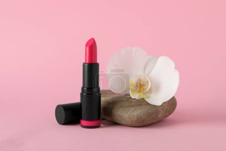 Photo for Beautiful lipstick and orchid flower on stone against pink background - Royalty Free Image