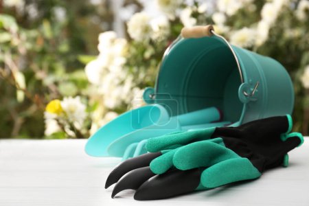 Photo for Gardening gloves and overturned bucket with different tools on white wooden table outdoors, space for text - Royalty Free Image