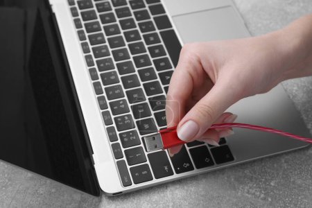 Photo for Woman holding USB cable near laptop at grey table, closeup - Royalty Free Image