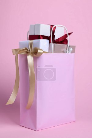 Foto de Color paper shopping bag full of gift boxes on pink background - Imagen libre de derechos