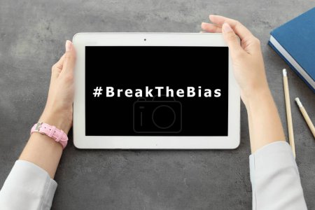 Photo for Woman holding tablet with hashtag BreakTheBias on screen at grey table, top view. Campaign theme for International Women's Day - Royalty Free Image