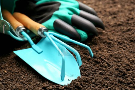 Photo for Overturned bucket with gardening tools and gloves on fresh soil, closeup - Royalty Free Image