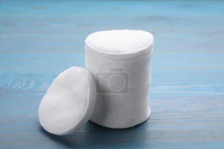 Stack of clean cotton pads on light blue wooden table, closeup