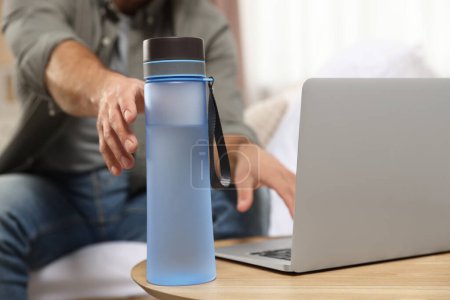 Téléchargez les photos : Man taking transparent plastic bottle of water while working on laptop at home, closeup - en image libre de droit