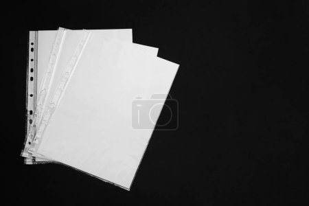 Foto de Punched pockets with paper sheets on black background, flat lay. Space for text - Imagen libre de derechos