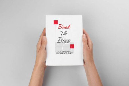Photo for Woman holding book with title Break The Bias devoted to International Women's Day against light grey background, closeup - Royalty Free Image