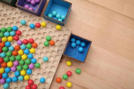 Wooden sorting board and boxes with colorful balls on table, flat lay. Montessori toy