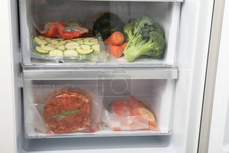 Téléchargez les photos : Sacs à vide avec différents produits au réfrigérateur. Stockage alimentaire - en image libre de droit