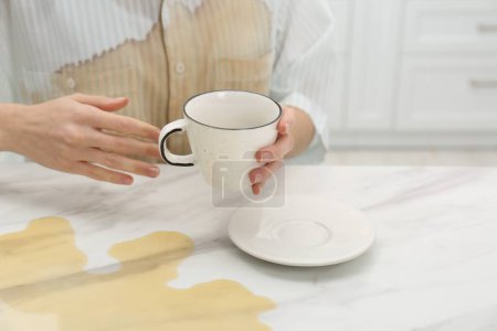 Frau mit verschüttetem Kaffee über ihrem Hemd am Marmortisch drinnen, Nahaufnahme