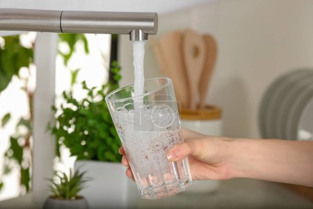 Foto de Woman filling glass with tap water from faucet in kitchen, closeup - Imagen libre de derechos