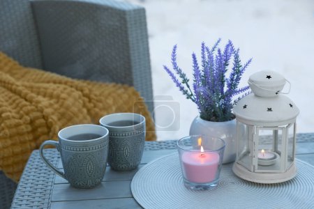 Téléchargez les photos : Bougie ardente, lanterne, fleurs en pot et tasses avec boisson chaude sur la table basse à l'extérieur. Cosy hiver - en image libre de droit