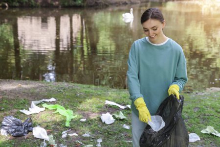 Young woman with plastic bag collecting garbage in park