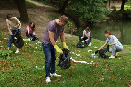 Téléchargez les photos : Groupe de personnes avec des sacs en plastique ramassant les ordures dans le parc - en image libre de droit