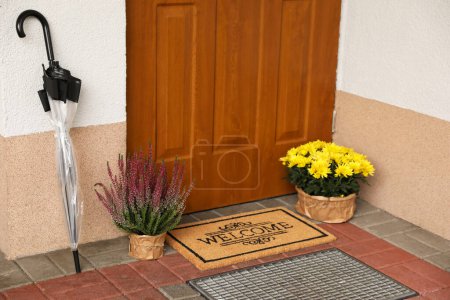 Foto de Door mat with word Welcome, umbrella and beautiful flowers near entrance - Imagen libre de derechos