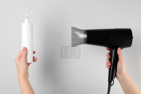 Photo for Woman holding spray bottle with thermal protection and hairdryer on white background, closeup - Royalty Free Image