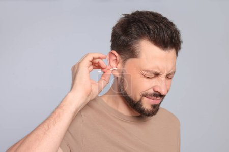 Photo for Man cleaning ears and suffering from pain on grey background - Royalty Free Image