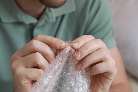 Photo for Man popping bubble wrap indoors, closeup view. Stress relief - Royalty Free Image