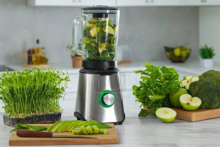Foto de Blender with ingredients for smoothie and products on white marble table in kitchen - Imagen libre de derechos
