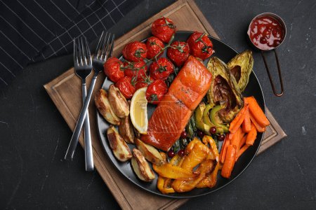 Foto de Sabroso salmón cocido y verduras servidas sobre mesa negra, puesta plana. Comidas saludables de la freidora - Imagen libre de derechos