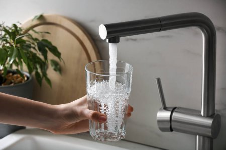 Photo for Woman filling glass with tap water from faucet in kitchen, closeup - Royalty Free Image