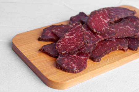 Pieces of delicious beef jerky on white textured table, closeup