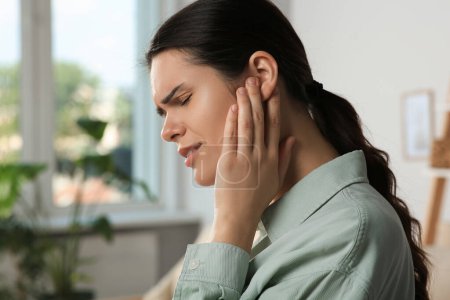 Young woman suffering from ear pain in room