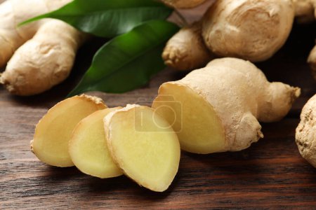 Photo for Cut and whole fresh ginger with leaves on wooden table, closeup - Royalty Free Image