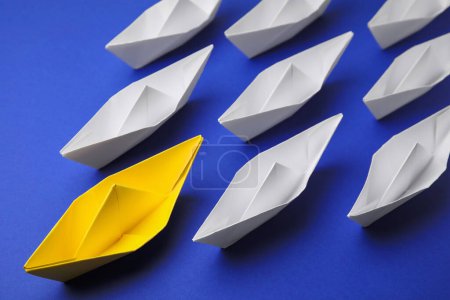 Yellow paper boat leading others on blue background, above view. Leadership concept