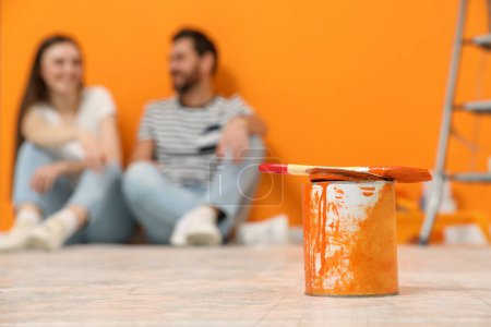 Photo for Designers sitting near freshly painted orange wall indoors, focus on can of paint - Royalty Free Image