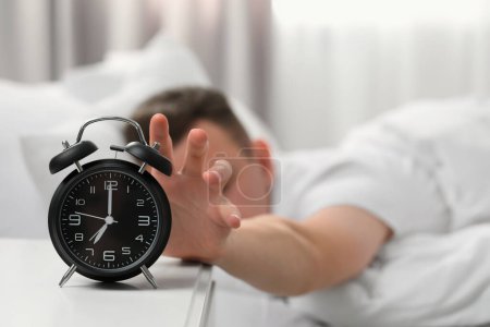 Man turning off alarm clock at home in morning, focus on hand. Space for text