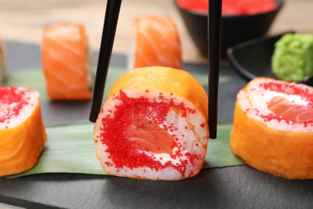 Foto de Taking delicious sushi roll with chopsticks at table, closeup - Imagen libre de derechos