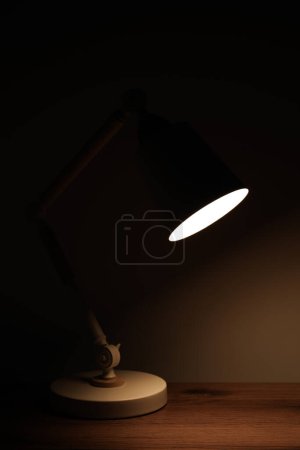 Téléchargez les photos : Stylish modern desk lamp on wooden table at night - en image libre de droit