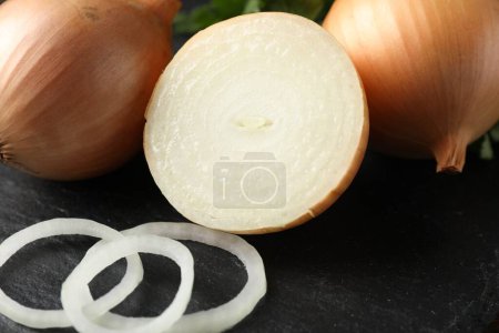 Foto de Whole and cut onions on black textured table, closeup - Imagen libre de derechos
