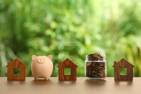 Photo for Piggy bank, jar of coins and house models on wooden table outdoors - Royalty Free Image