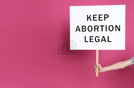 Foto de Woman holding placard with phrase Keep Abortion Legal on pink background, closeup. Abortion protest - Imagen libre de derechos