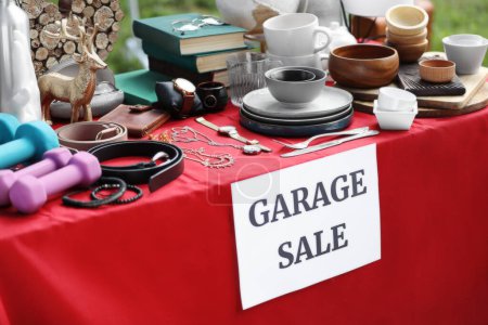 Téléchargez les photos : Paper with sign Garage sale and many different items on red tablecloth outdoors - en image libre de droit
