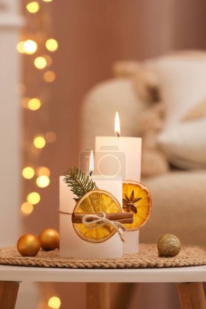 Foto de Hermosas velas encendidas decoradas con rebanadas de naranja seca y palitos de canela en la mesa blanca en el interior. Ambiente navideño - Imagen libre de derechos